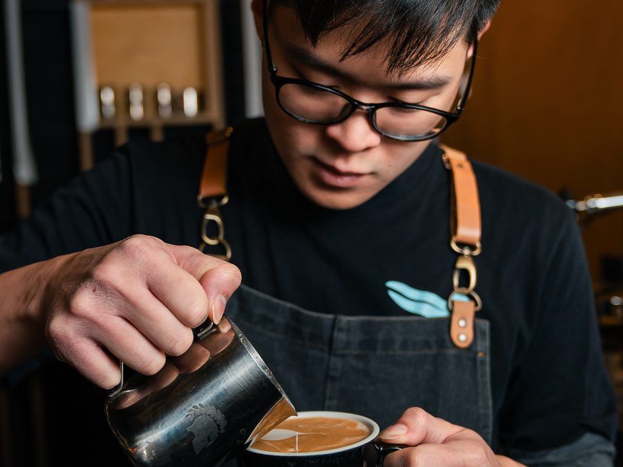 Barista gießt Milch in einen Kaffee
